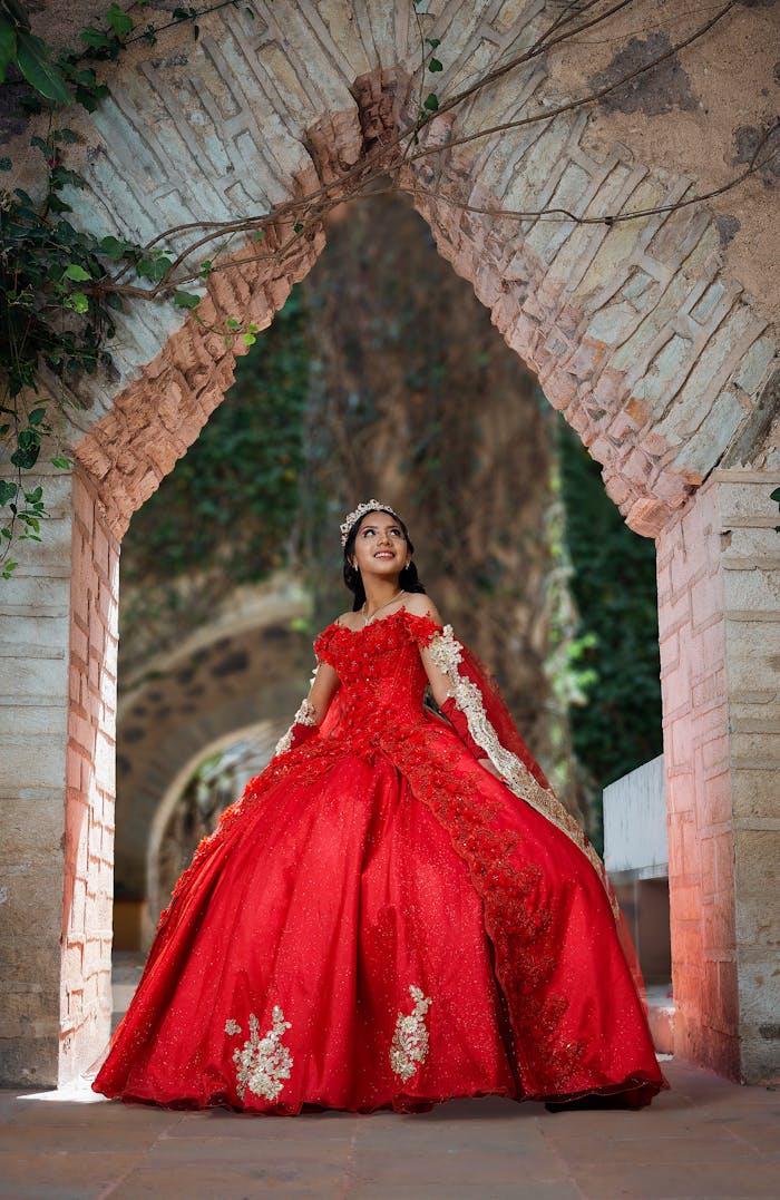 Young woman in red quinceañera dress poses in historic Guanajuato archway, Mexico.