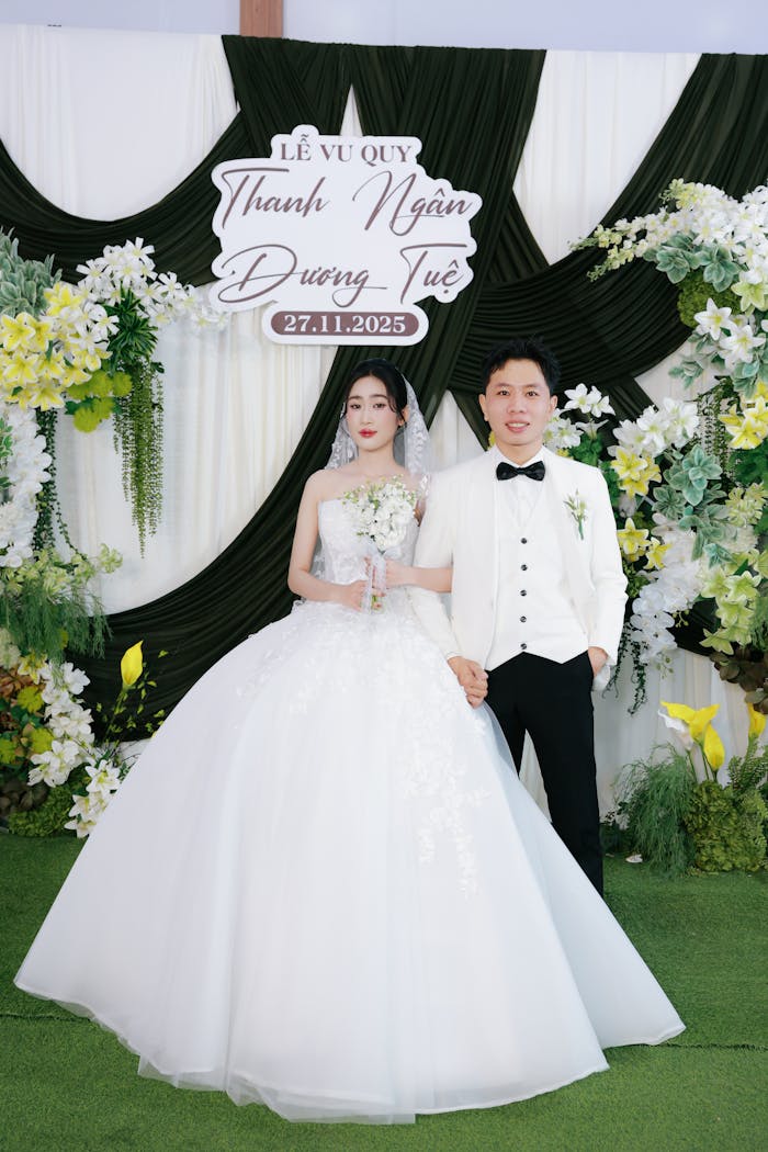 An elegant wedding couple poses with floral backdrop for their special day.